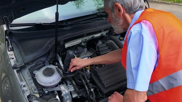 Senior Man Wears Warning Vest and Controls Engine of the Car - Closeup