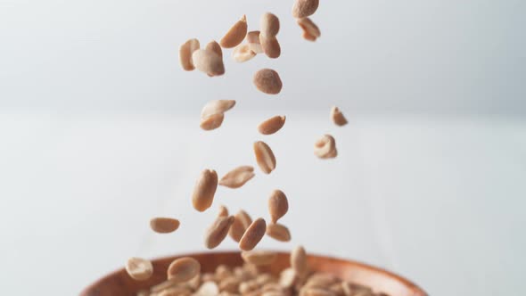 Camera follows salted peanuts falling into a bowl. Slow Motion.