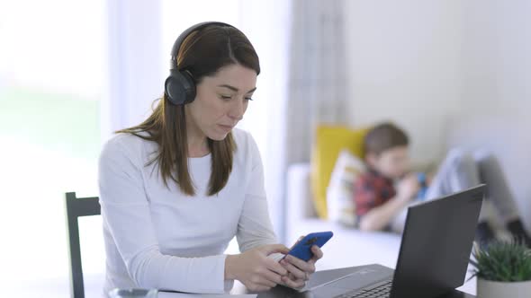 Mother working from home with son sitting in background