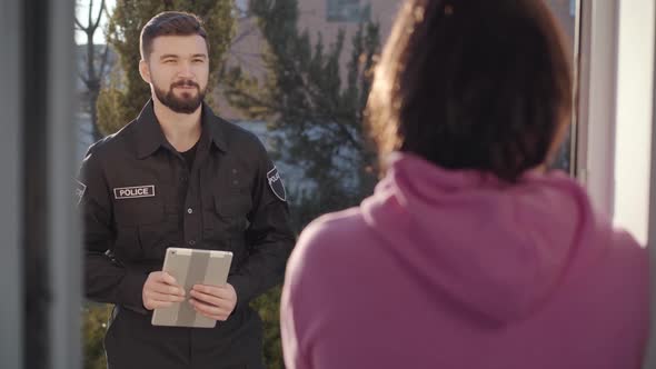 Portrait of Handsome Caucasian Police Officer Standing with Tablet at Entrance Door and Talking 