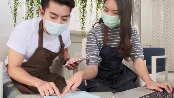 Asian couple in masks doing business calculations of restaurant and checking bills