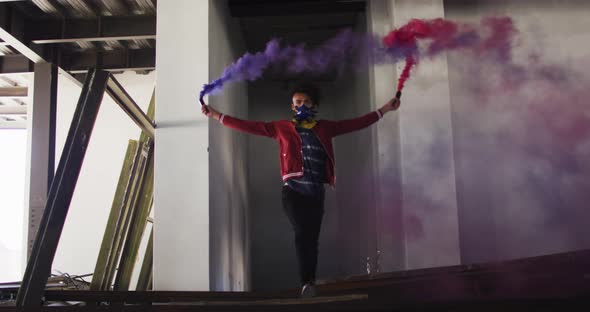 Mixed race man holding blue and purple flares walking through an empty building