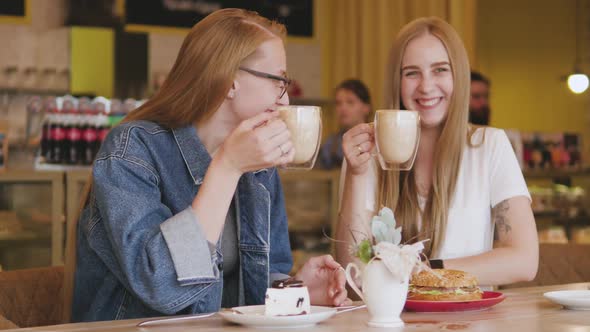 Two Young Attractive Women Have Breakfast in a Cafe. Two Friends Are Drinking Coffee