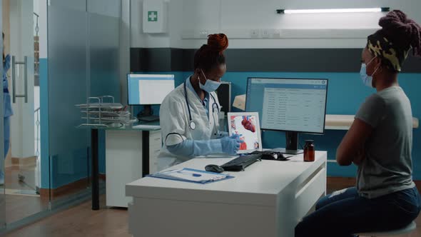 Medic with Face Mask Pointing at Tablet with Heart Figure