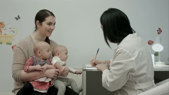 Cute Newborn Twins Being Examine By Pediatrician with Toy