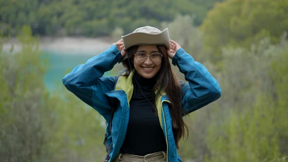 Young Darkhaired Explorer Woman in Nature Puts on Hat and Smiles