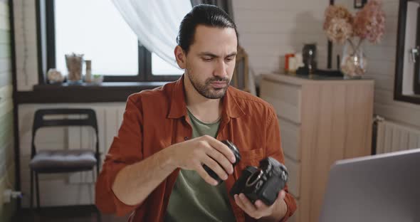 The Photographer Puts the Lens on the Camera While Sitting in Front of a Laptop