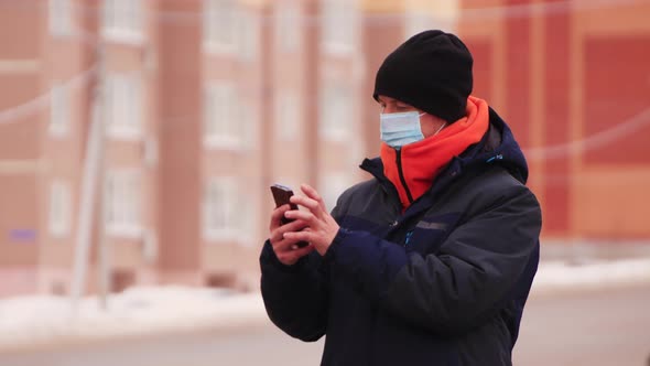 Closeup of a Man in a Medical Mask Makes Purchases Online on a Smartphone