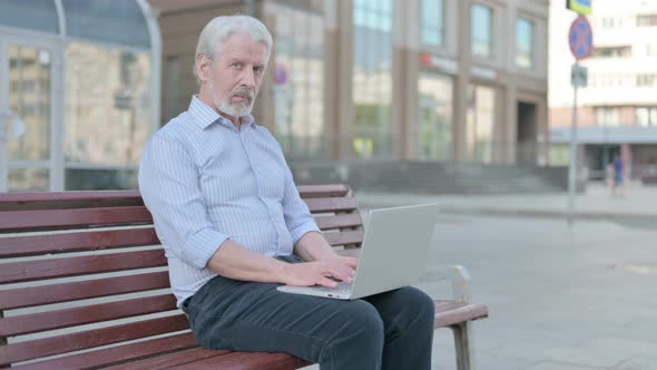 Old Man with Laptop Looking at Camera While Sitting Outdoor on Bench