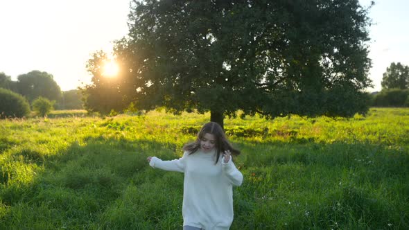 Happy little girl is playing and running in the field next to a lonely tree