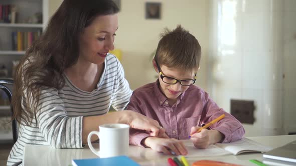 Young Mother and Son Doing Homework and Sitting at Table in Home Interior During Quarantine Spbd