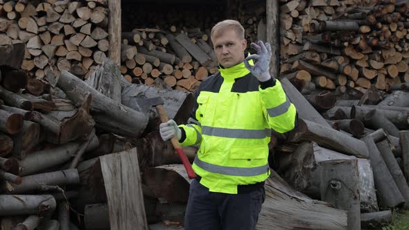 Lumberjack in Reflective Jacket. Man Woodcutter Hold Small Axe, Show Ok Sign. Sawn Logs, Firewood