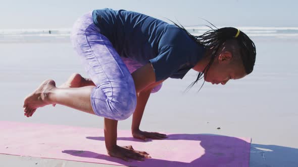 African American woman doing yoga position on the beach and blue sky background