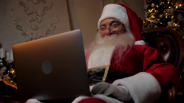 Smiling Modern Santa Claus Uses Laptop Fills in Holiday Cards for Children