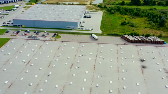 Aerial following shot of semi-trailer trucks travelling along a warehouse on the parking lot in the