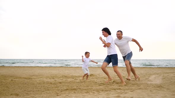 A Happy Family of Three Running Around Each Other on a Sandy Sea Beach, in Slow Motion.