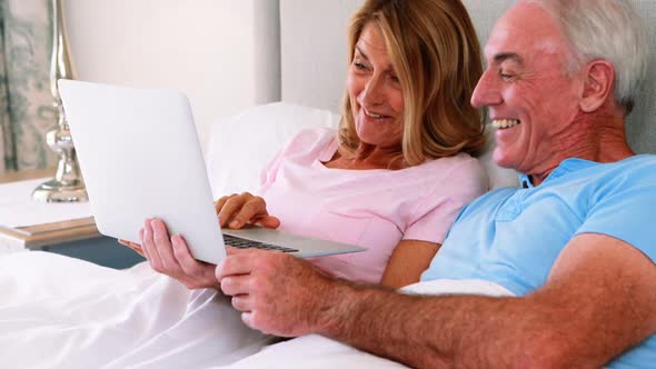 Happy senior couple on bed using laptop