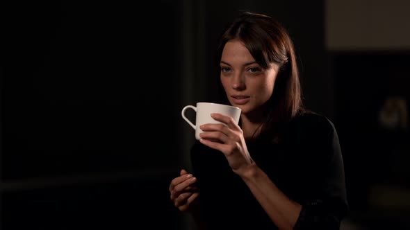 Young and Beautiful Brunette Woman Is Drinking Tea or Coffee From Big White Cup, Sitting in Studio