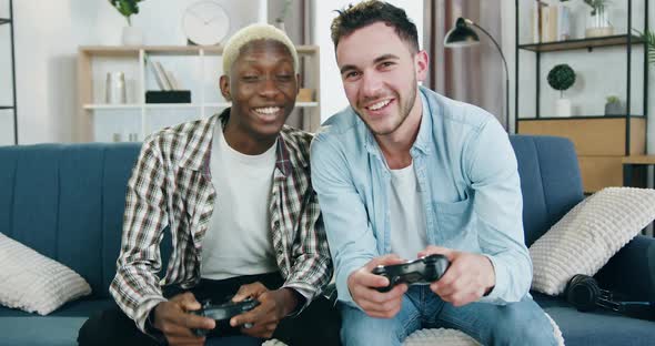 Mixed Race Young Gay Couple in Love which Sitting on the Couch at Home and Playing Videogames
