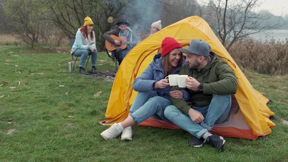 Ouple Camps in Nature with Campfire and Drinks Beverage From Vintage White Cups