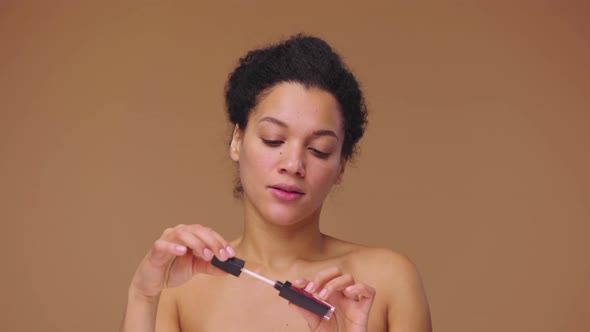 Beauty Portrait of Young African American Woman Unrolling Lip Gloss Examines Brush Twirls It Back