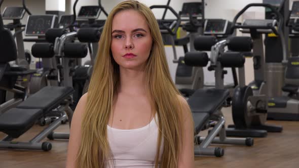 A Young Beautiful Woman Looks at the Camera in a Gym