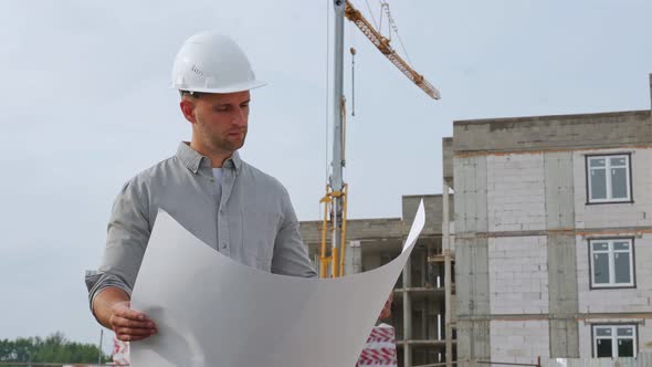 An Architect in a Hard Hat Managing a Project Standing with Drawings on a Construction Site