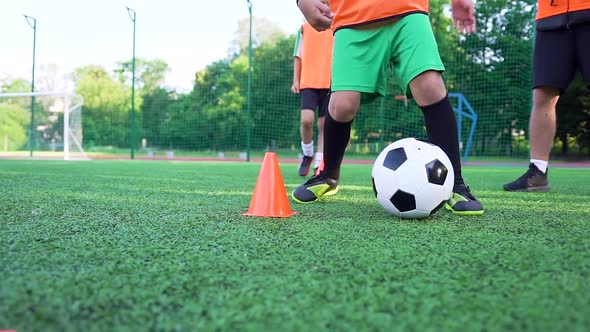 Boy in Football Uniform Training with Ball Around Small Racks to Improve His Speed During Workout