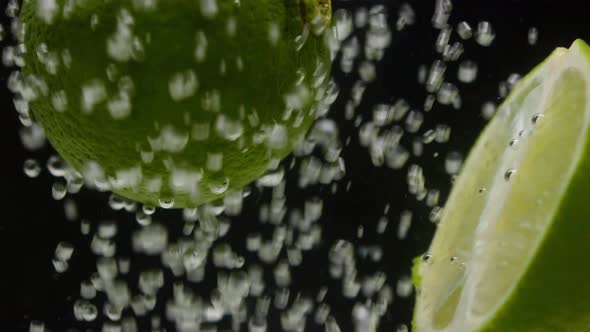 Closeup of Falling Ripe Limes Into the Sparkling Water on Black Background Making a Cocktail of