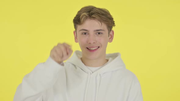 Young Man Pointing at Camera Inviting on Yellow Background