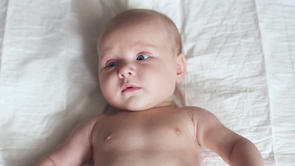 Happy Newborn Baby Toddler on Bed, Moves Hands, Smiles and Tries To Talk