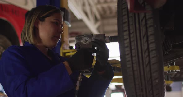 Female mechanic changing tires of the car using a power drill at a car service station