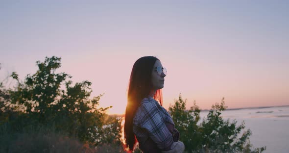 A young girl on the background of sunset looks thoughtfully into the distance