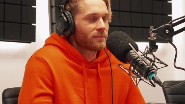 Blond young man talking into microphone while recording radio show