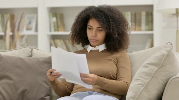 Young African Woman Reading Documents on Sofa