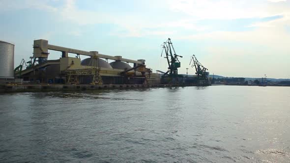 Boat going by sea, approaching wharf with immense storehouses and cranes at port