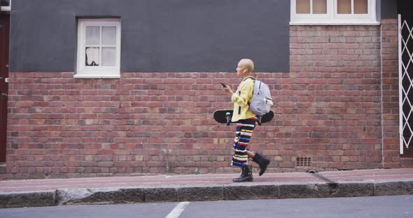 Mixed race woman walking on street holding her skateboard and her phone