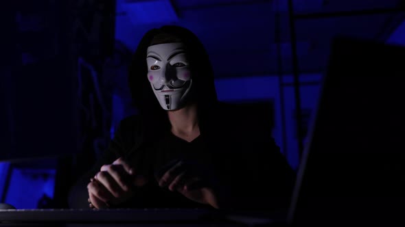 Portrait of Unrecognizable Hacker Man Wearing Anonymous Mask Starting Breaking Computer System and