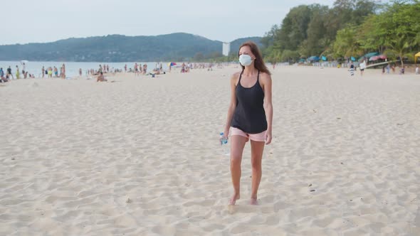 Woman in a Protective Face Mask Walking on the Beach