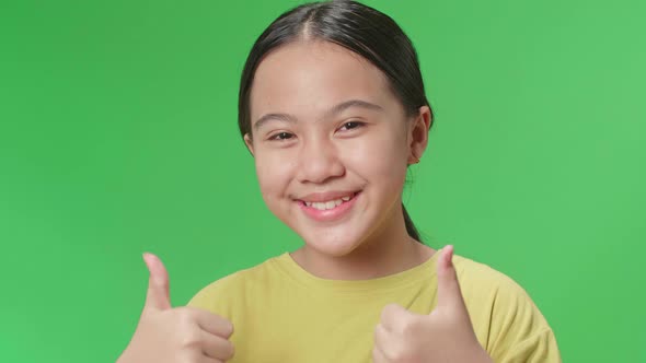 Happy Young Asian Kid Girl Showing Thumbs Up Gesture While Standing In The Green Screen Studio alt