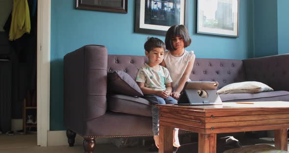 Brother and sister at home during Coronavirus lockdown, sitting on sofa, watching a movie on digital