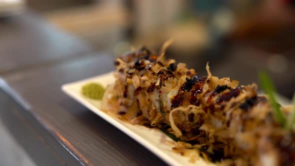 On the foreground we see a plate with sushi. On the background chef is doing some preparations.