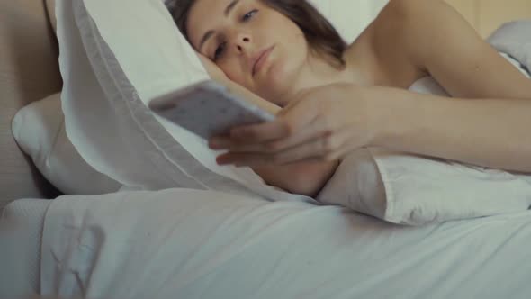 Girl under blanket surfing phone in bed