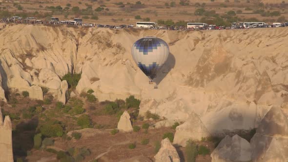 Hot Air Balloon with Blue White Envelope Hangs Near Cliff