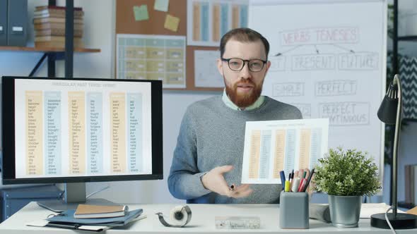 Portrait of Online English Tutor Recording Video for Vlog Holding Charts and Pointing at Computer alt