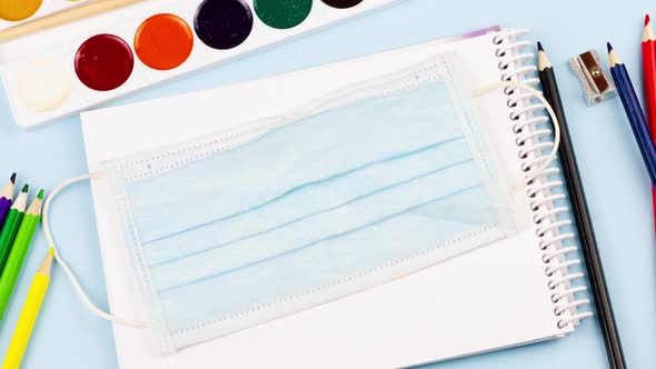 School Supplies with a Notepad Lie on a Pastel Blue Background with a Medical Mask