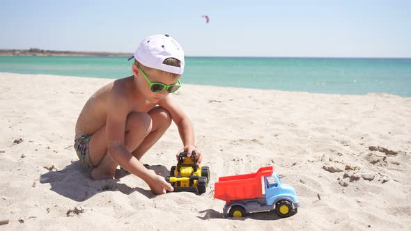 Cute Boy Playing with Sand on the Beach with Plastic Cars, Toys