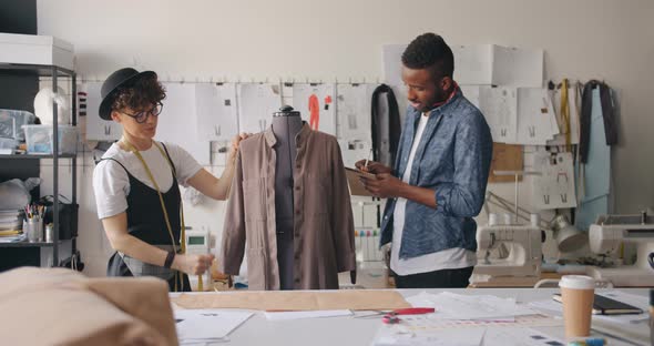 Female Tailor Measuring Garment While Man Writing in Notebook Talking Smiling