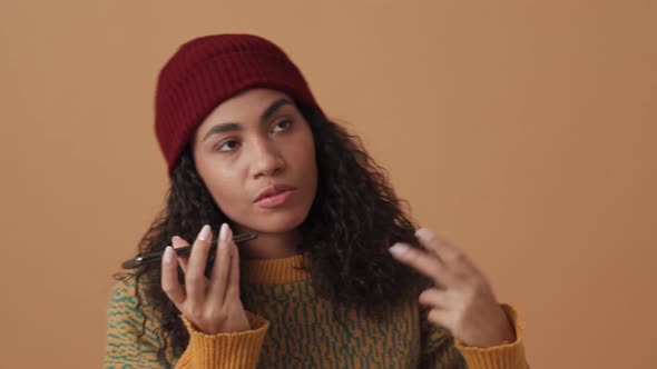 Positive African curly-haired woman recording voice message by phone