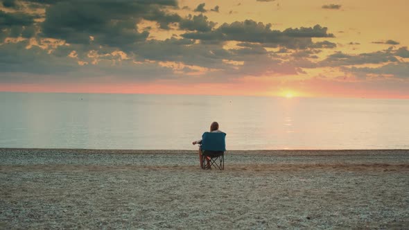 Back View of Girl Admiring Sunset on the Sea Sitting in Folding Tourist Chair